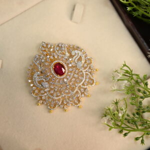 The image shows a beautiful pendant set against a backdrop of a brown velvet box and delicate white flowers. The pendant itself is a stunning piece of jewelry, featuring a large, oval-shaped red gemstone surrounded by a halo of sparkling white stones. The design is intricate and ornate, with delicate filigree work and a gold-colored setting. The overall effect is one of elegance and sophistication.