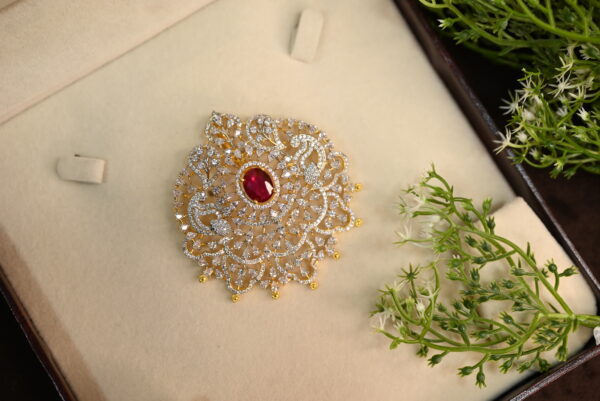 The image shows a beautiful pendant set against a backdrop of a brown velvet box and delicate white flowers. The pendant itself is a stunning piece of jewelry, featuring a large, oval-shaped red gemstone surrounded by a halo of sparkling white stones. The design is intricate and ornate, with delicate filigree work and a gold-colored setting. The overall effect is one of elegance and sophistication.