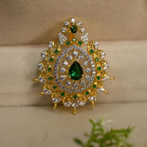The image shows a gold pendant with a teardrop-shaped green stone, possibly an emerald or a green CZ diamond, in the center. The pendant is adorned with smaller white stones, likely diamonds or CZ diamonds, creating a shimmering halo around the central green stone.