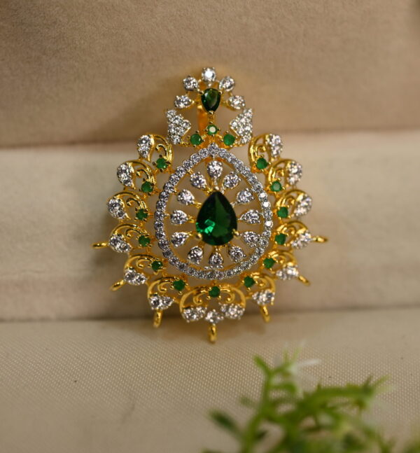 The image shows a gold pendant with a teardrop-shaped green stone, possibly an emerald or a green CZ diamond, in the center. The pendant is adorned with smaller white stones, likely diamonds or CZ diamonds, creating a shimmering halo around the central green stone.