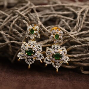 The background of the image is a neutral color, likely to highlight the earrings. There appears to be a small sprig of greenery in the bottom right corner of the image, adding a natural touch.