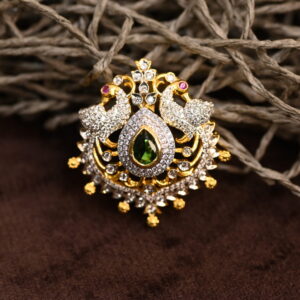 Two peacocks face each other, their bodies forming a circular frame. The peacocks are adorned with white stones, possibly cubic zirconia (CZ), which sparkle and catch the light. The pendant showcases a rich color palette with a deep green gemstone at the center, surrounded by white CZ stones and a golden frame.