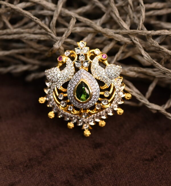 Two peacocks face each other, their bodies forming a circular frame. The peacocks are adorned with white stones, possibly cubic zirconia (CZ), which sparkle and catch the light. The pendant showcases a rich color palette with a deep green gemstone at the center, surrounded by white CZ stones and a golden frame.
