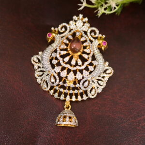 The image shows a beautiful CZ pendant featuring a pair of peacocks with a large, round ruby in the center. The peacocks are adorned with white CZ stones, creating a dazzling and intricate design. A small, bell-shaped pendant hangs from the bottom, adding a touch of elegance. The overall effect is a luxurious and eye-catching piece of jewelry.