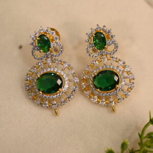 The background of the image is a neutral color, likely to highlight the earrings. There appears to be a small sprig of greenery in the bottom right corner of the image, adding a natural touch.
