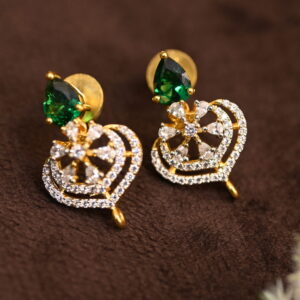 The background of the image is a neutral color, likely to highlight the earrings. There appears to be a small sprig of greenery in the bottom right corner of the image, adding a natural touch.