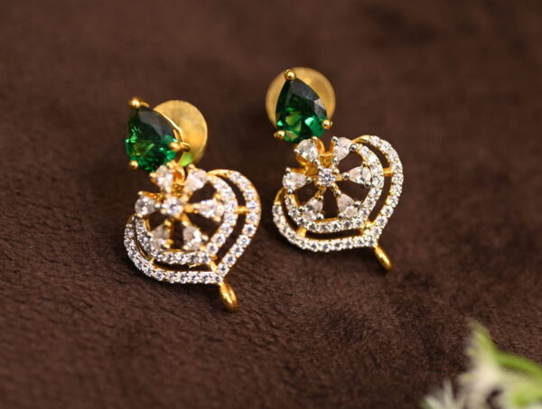 The background of the image is a neutral color, likely to highlight the earrings. There appears to be a small sprig of greenery in the bottom right corner of the image, adding a natural touch.