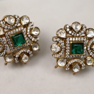 The image shows a pair of earrings. They have a square-shaped center with a large green gemstone in the middle. Surrounding the green gemstone are smaller white gemstones arranged in a circular pattern. The earrings are made of gold.