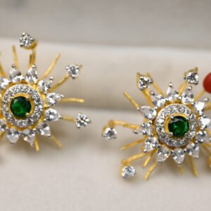 The image showcases an exquisite pair of earrings with a vibrant and intricate design. The earrings are crafted in a starburst pattern, featuring a radiant green gemstone at the center, encircled by sparkling white stones. The outer structure is adorned with golden rays, extending outward like the beams of the sun, each tipped with small, brilliant white stones, adding a touch of sparkle and depth.