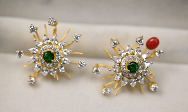 The image showcases an exquisite pair of earrings with a vibrant and intricate design. The earrings are crafted in a starburst pattern, featuring a radiant green gemstone at the center, encircled by sparkling white stones. The outer structure is adorned with golden rays, extending outward like the beams of the sun, each tipped with small, brilliant white stones, adding a touch of sparkle and depth.
