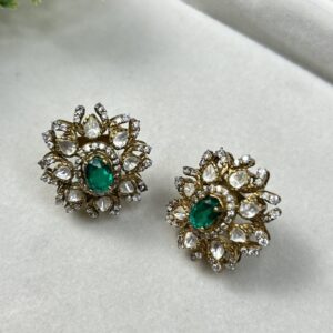 "Close-up of a pair of elegant gold stud earrings with a delicate floral design. Each earring is adorned with a cluster of sparkling moissanites surrounding a captivating emerald-cut green gemstone."
