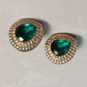 The image shows a pair of elegant earrings. Each earring features a large, pear-shaped emerald-green gemstone as the centerpiece. The gemstones are surrounded by a halo of smaller, round-cut white stones, creating a dazzling frame. The earrings appear to be set in a warm-toned metal, possibly gold or brass.