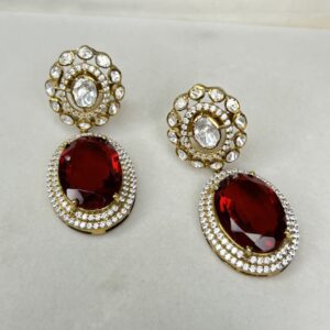 The image shows a pair of elegant dangle earrings. Each earring features a large, oval-shaped red gemstone surrounded by a halo of smaller white gemstones. The top of each earring has a circular design with multiple layers of white gemstones.
