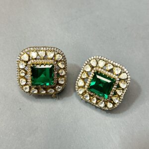 The image shows a pair of stunning earrings. They are made of gold and feature a large, square-cut emerald gemstone in the center. The emerald is surrounded by a halo of smaller, white gemstones, possibly diamonds. The earrings have a delicate, intricate design with a floral pattern. The overall effect is one of elegance and luxury.