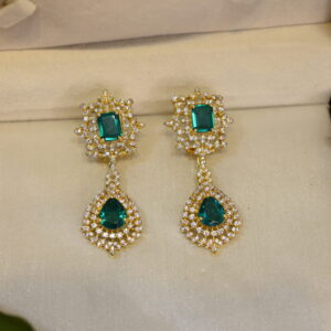 The image shows a pair of elegant drop earrings resting inside a jewelry box. The earrings are made of gold-plated 925 sterling silver and feature a cluster of sparkling moissanite stones.