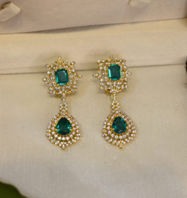 The image shows a pair of elegant drop earrings resting inside a jewelry box. The earrings are made of gold-plated 925 sterling silver and feature a cluster of sparkling moissanite stones.