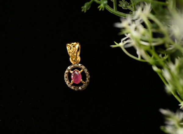 The image shows a close-up of a delicate pendant necklace. The pendant is made of 925 silver and features a central oval-shaped ruby gemstone. The ruby is surrounded by a circular halo of smaller diamonds, creating a dazzling contrast. The pendant hangs from a thin silver chain, and the background is a dark color, possibly black velvet, which makes the pendant stand out even more.
