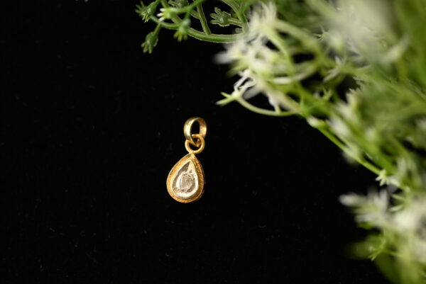 The pendant appears to be handcrafted, given the slightly uneven edges and rustic charm. The black background and delicate greenery in the image enhance the pendant's beauty and create a sense of luxury.