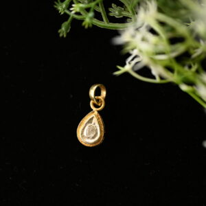 The image shows a close-up of a delicate gold pendant hanging from a thin chain. The pendant is shaped like a teardrop and holds a single, round diamond in its center. The diamond is clear and sparkling, reflecting light beautifully. The background of the image is dark, creating a dramatic contrast that highlights the pendant's elegance.