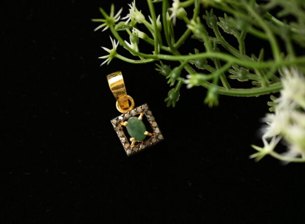 The image showcases a delicate and elegant pendant featuring a square design with a central green stone and a halo of diamonds. It appears to be crafted with attention to detail and would make a beautiful addition to any jewelry collection.