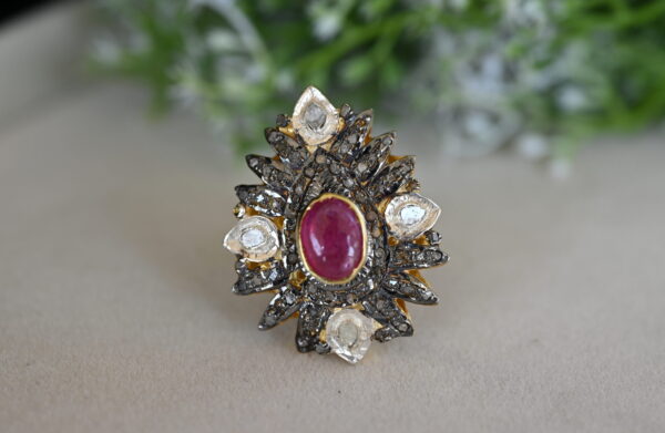 The image showcases a vintage-style ring. The ring features a central oval-shaped ruby, surrounded by a cluster of smaller diamonds. The diamonds are set in a pave setting, creating a dazzling effect. The ring band is made of 925 sterling silver and displays a unique floral motif with intricate detailing.