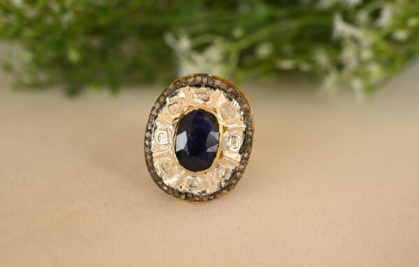 The image you sent shows a beautiful ring with a large, oval-shaped blue sapphire as the center stone. The sapphire is a deep, rich blue color and appears to be of high quality. It's surrounded by a halo of smaller diamonds, which add sparkle and enhance the sapphire's brilliance. The ring's band looks to be made of gold, possibly yellow gold, and it has intricate details like small diamonds or milgrain.