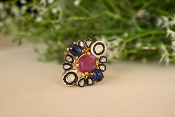 The image provides a close-up view, allowing for a detailed appreciation of the craftsmanship and the interplay of colors and textures. The background is blurred, drawing attention to the ring and its intricate details. "Ruby & Sapphire Cluster Ring"