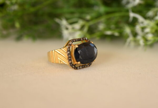 The image you sent shows a vintage-style ring with a large, oval-shaped sapphire as the centerpiece. The sapphire has a deep blue color and is surrounded by a halo of smaller diamonds. The ring band appears to be made of gold and features a wide, textured design. The ring looks quite substantial and luxurious.