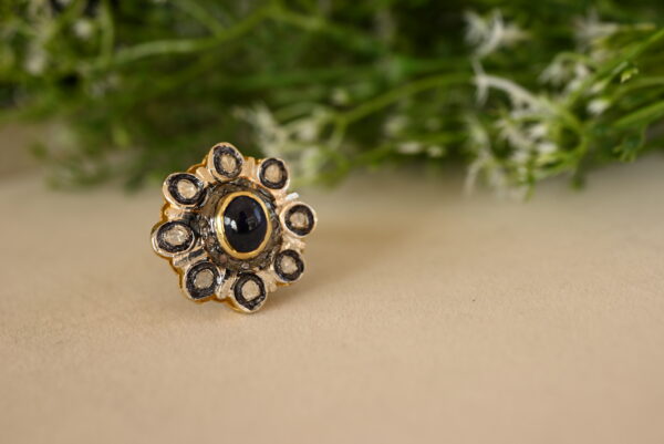 The image shows a pair of elegant, pierced earrings. The earrings feature a large, clear crystal that hangs delicately from a black metal setting. The metal appears to be intricately designed with a geometric pattern. The background is blurred, suggesting that the earrings are being photographed on a surface or in a setting that is not the primary focus.