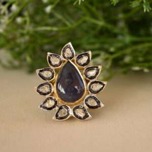 The image shows a ring with a large, pear-shaped blue gemstone, likely a sapphire, surrounded by a halo of smaller diamonds. The ring appears to be made of silver or gold and has intricate floral designs. It's a beautiful and elegant piece of jewelry.