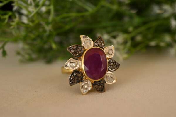 The image showcases a stunning ring set against a backdrop of lush green foliage. The ring features a large, oval-shaped ruby as its centerpiece, radiating a deep, rich red hue. Surrounding the ruby is a halo of smaller, round diamonds, creating a dazzling contrast of color and sparkle.