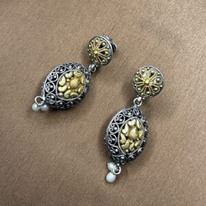 "A close-up of a pair of black and gold fusion earrings. The earrings have a round, ornate design with a central gold motif. Delicate pearls hang from the bottom of each earring."