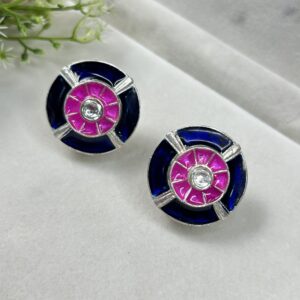 The image shows a pair of oval-shaped stud earrings with a unique design. Colors: The earrings feature a striking color combination of deep blue, vibrant pink, and white. Design: The central part of each earring has a white stone, surrounded by a circular pink enamel inlay. This pink circle is then framed by a wider band of deep blue enamel. Material: The earrings appear to be made of silver metal.
