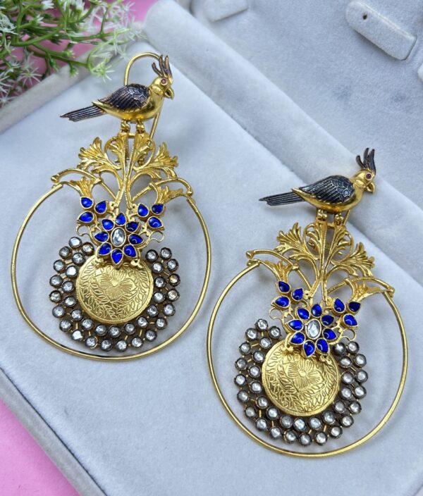 The image showcases a pair of exquisite fusion earrings. They appear to be handcrafted with a blend of traditional Indian motifs and contemporary design elements. Shape: The earrings have a circular base with intricate silver-toned detailing.