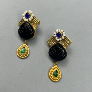 The image shows a pair of statement earrings. They have a unique and intricate design with a mix of gold-toned metal, black onyx, green gemstones, and pearls. One earring features a geometric shape, while the other has a more organic, leaf-like shape. Both earrings have a dangling element with a green gemstone and a gold-toned embellishment.