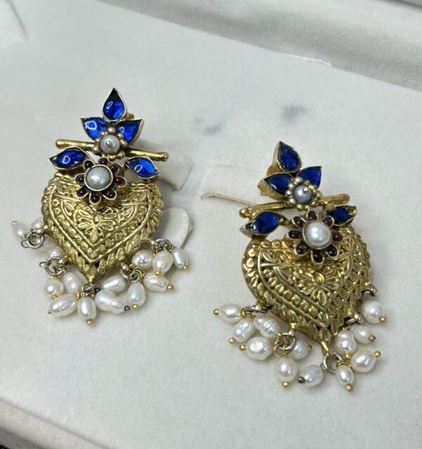 Intricate Detailing: The heart is covered in intricate gold-toned filigree work, creating a delicate and textured surface. Gemstones: Several small, round blue gemstones are set within the filigree work, adding a pop of color. Pearls: Clusters of small, white pearls hang below the heart, creating a dangling effect.