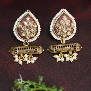 The image showcases a pair of elegant fusion earrings. They feature a teardrop-shaped pendant adorned with a beautiful floral motif in a rich, warm shade of purple. The intricate detailing of the flowers is truly captivating, with each petal meticulously crafted and embellished with sparkling white stones.