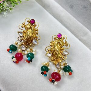 This image shows a pair of ornate, traditional Indian earrings. The earrings are gold-toned with intricate peacock designs, embedded with white stones and topped with a round pink gem. They are adorned with hanging green and pink beads, tiny pearls, and multicolored accent beads, giving them a festive and vibrant look.