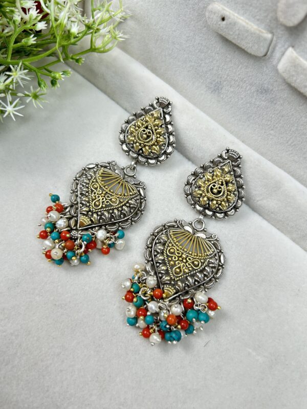These are ornate, traditional-style earrings made of oxidized silver with gold detailing. They feature teardrop shapes and colorful dangling beads in turquoise, red, and white. Perfect for ethnic or festive wear.