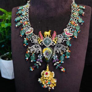 The image shows a beautiful necklace with a fusion of traditional and contemporary styles. Central Motif: The centerpiece features a large, ornate pendant with a blend of geometric patterns and floral motifs. It is adorned with a variety of colorful gemstones, including emeralds, rubies, and pearls.