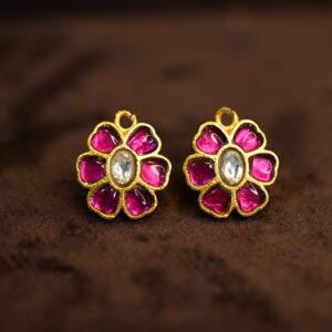 The image shows a pair of earrings. They are made of gold with a floral design. The flowers are decorated with pink and white stones. The earrings appear to be made in the Kundan style, a traditional Indian jewelry-making technique.