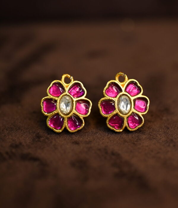 The image shows a pair of earrings. They are made of gold with a floral design. The flowers are decorated with pink and white stones. The earrings appear to be made in the Kundan style, a traditional Indian jewelry-making technique.