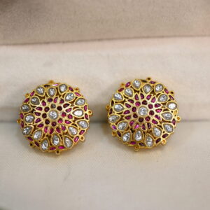 The image shows a pair of elegant Kundan earrings. The earrings are circular in shape and feature a central motif adorned with sparkling white Kundan stones. These stones are set in a delicate gold-plated frame. Surrounding the central motif is a band of vibrant pink stones, adding a pop of color. The earrings are secured with a post and back closure.