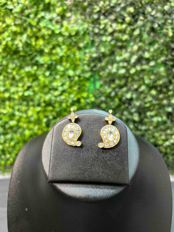 The image shows a pair of delicate earrings. They are made of gold or a gold-toned metal and feature a design with small, sparkling white stones set in a circular pattern. The earrings appear to be lightweight and have a simple, elegant style.