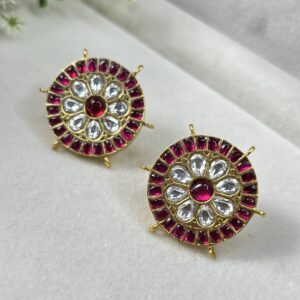 The image showcases a pair of exquisite Kundan earrings. The earrings are circular in shape and feature a central floral motif adorned with white Kundan stones. Surrounding the floral motif is a circular border of red Kundan stones, creating a striking contrast. The earrings are suspended from delicate gold-toned loops. The overall design evokes a sense of elegance and traditional Indian craftsmanship. "Kundan Spark Studs Earring"