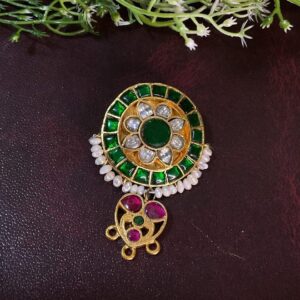 The image showcases a stunning Kundan pendant set against a dark background. The pendant features a circular design with a central, large Kundan stone surrounded by a halo of smaller green Kundan stones. The pendant is further embellished with delicate pearls and ruby accents, adding to its overall charm.