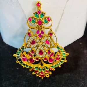 The image showcases a beautiful and ornate piece of jewelry, likely a pendant or a part of a larger necklace. It appears to be crafted using the traditional Indian technique of Kundan work, where precious and semi-precious stones are set in gold foil.