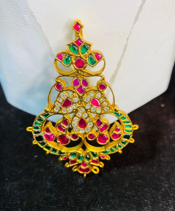 The image showcases a beautiful and ornate piece of jewelry, likely a pendant or a part of a larger necklace. It appears to be crafted using the traditional Indian technique of Kundan work, where precious and semi-precious stones are set in gold foil.