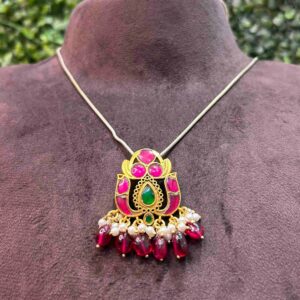 The image appears to showcase a traditional Indian necklace, likely a Harsali. It features a central pendant with a peacock motif, a common symbol of grace and beauty in Indian culture. The peacock's body is adorned with intricate gold work and studded with colorful gemstones, possibly rubies, emeralds, and diamonds.
