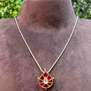 The image shows a close-up of a delicate necklace with a pendant. The pendant is the focal point of the image. It has a crescent moon shape. The moon is adorned with intricate Kundan work, featuring small, colorful gemstones. The overall color scheme seems to be a combination of gold and silver.